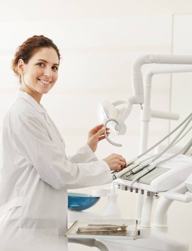 Waist up portrait of confident female dentist smiling at camera while adjusting dental chair , copy space